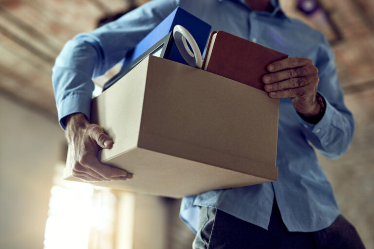 Homem com caixa de pertences de sua mesa de trabalho deixando a empresa representando turnover e quiet quitting.