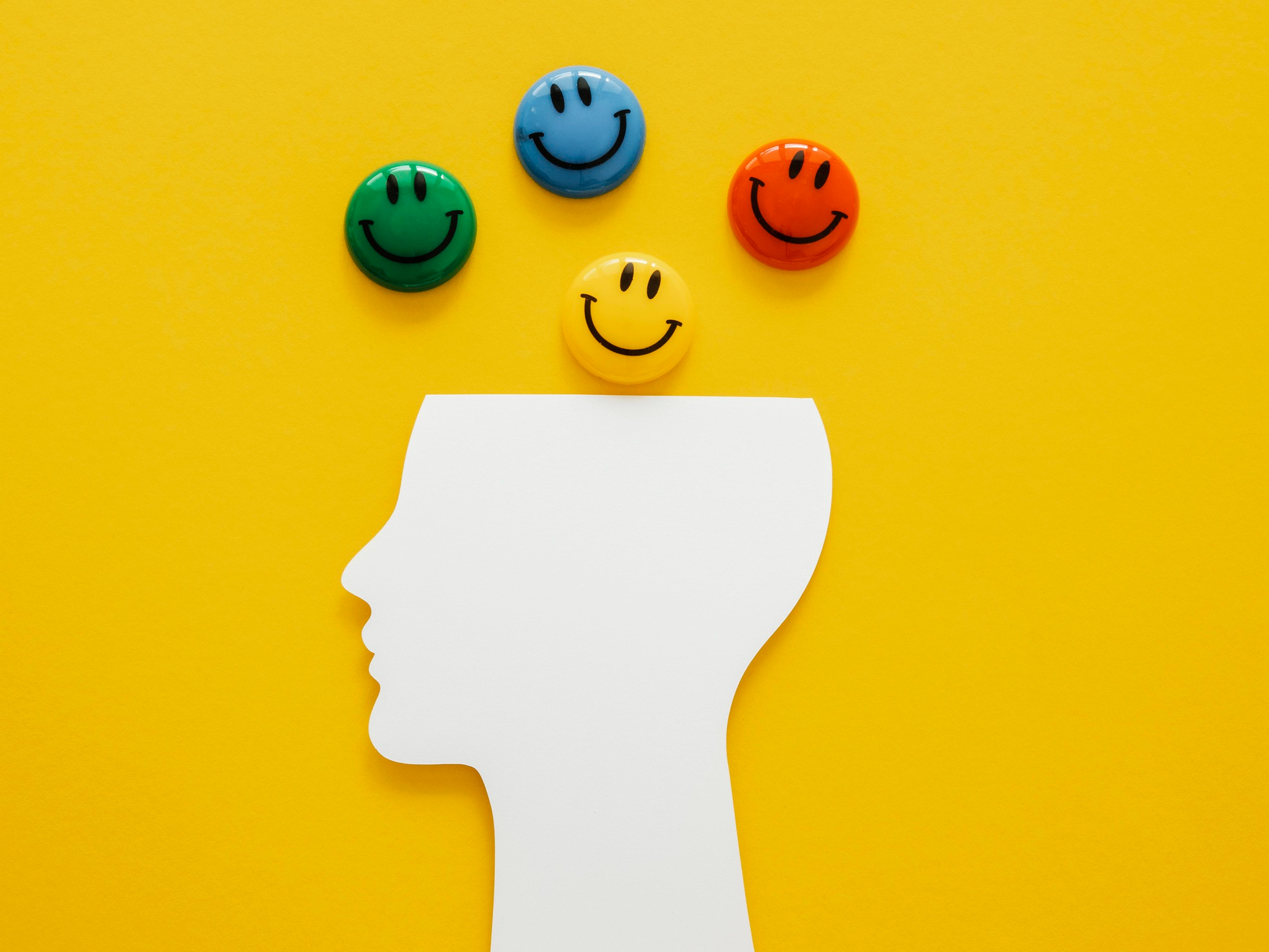 Contorno de uma cabeça com emojis coloridos em cima representando a inteligência emocional.