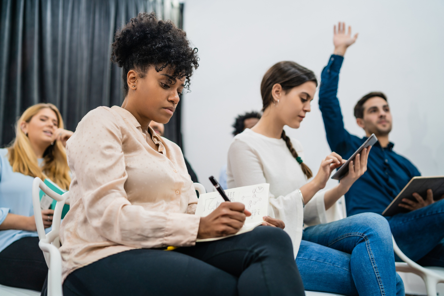 Participantes em treinamento, com uma pessoa anotando no caderno e outra levantando a mão durante uma atividade de transferência de treinamento.