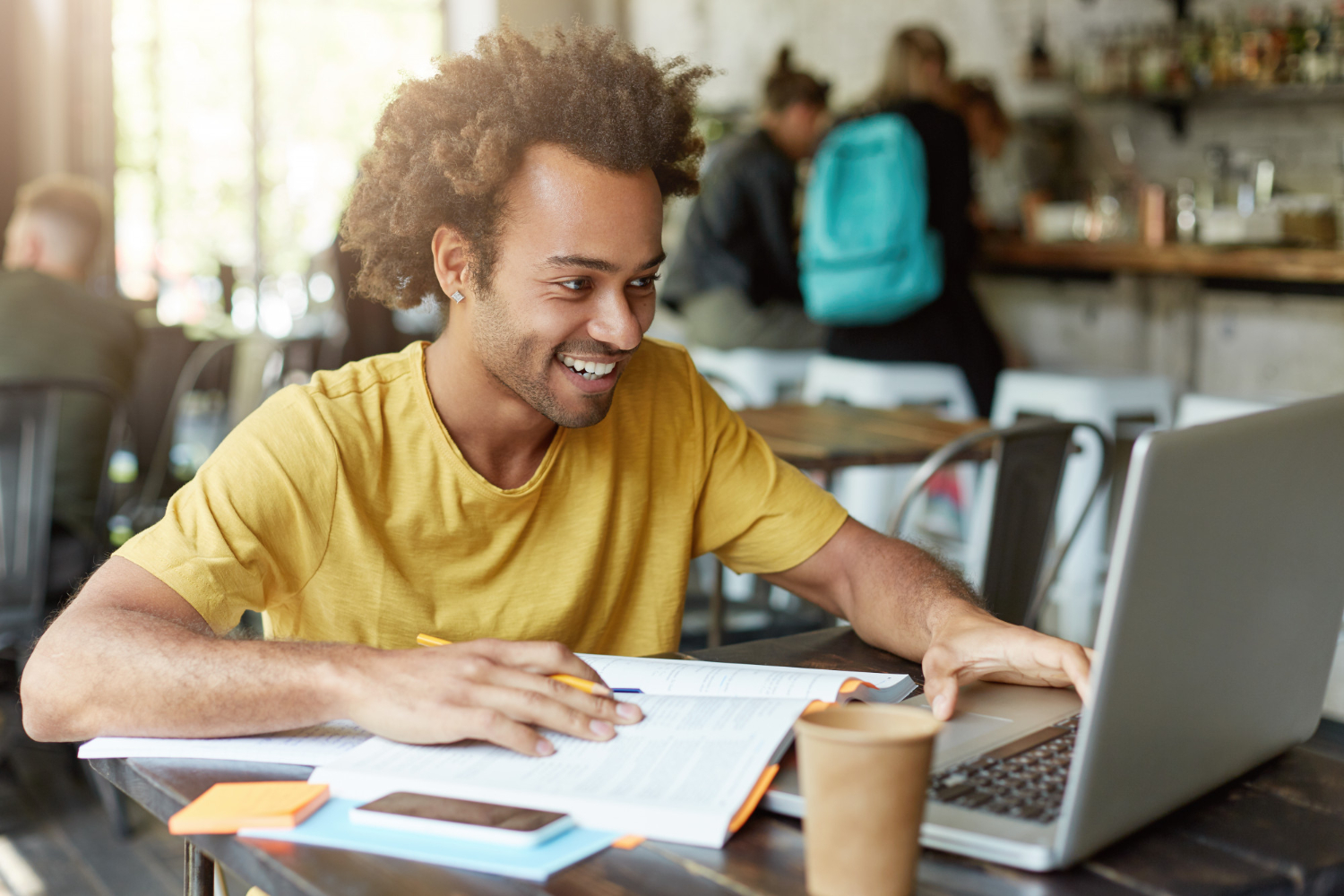 Homem estudando em um notebook, com livros e materiais sobre a mesa, em um ambiente que estimula a cultura de aprendizagem.