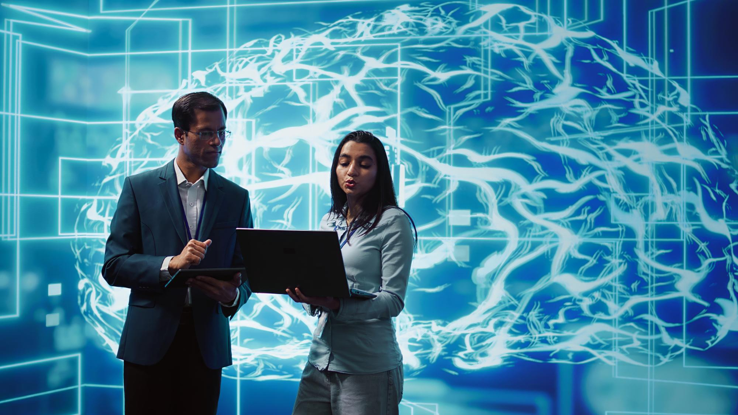 Dois profissionais analisam informações em dispositivos digitais diante de uma representação gráfica de um cérebro conectado por redes luminosas. A imagem simboliza a integração entre liderança e inteligência artificial, destacando tomada de decisão, colaboração humana e uso estratégico de tecnologia no ambiente corporativo.